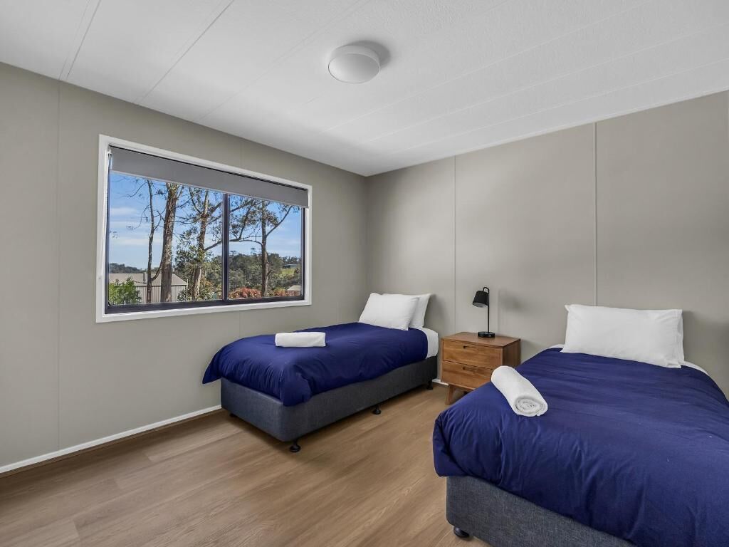 Un dormitorio moderno con dos camas, un ventanal grande y una mesita de noche.
