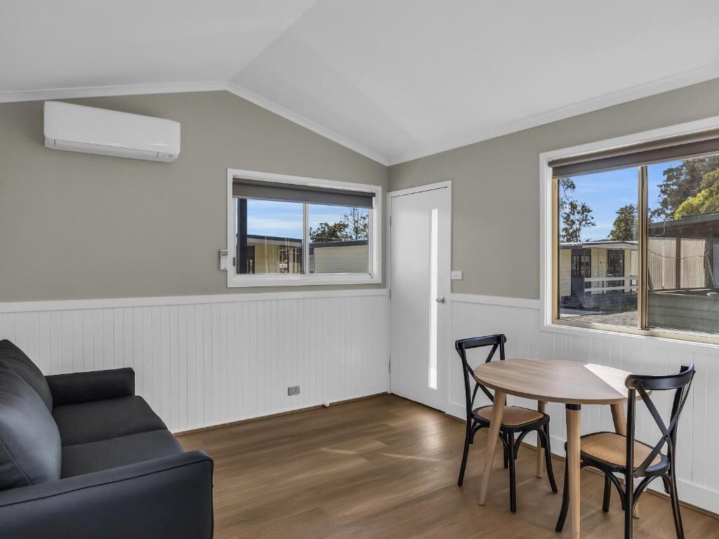 A room with a dining table, chairs, a black sofa, a window with a view, and an air conditioning unit.