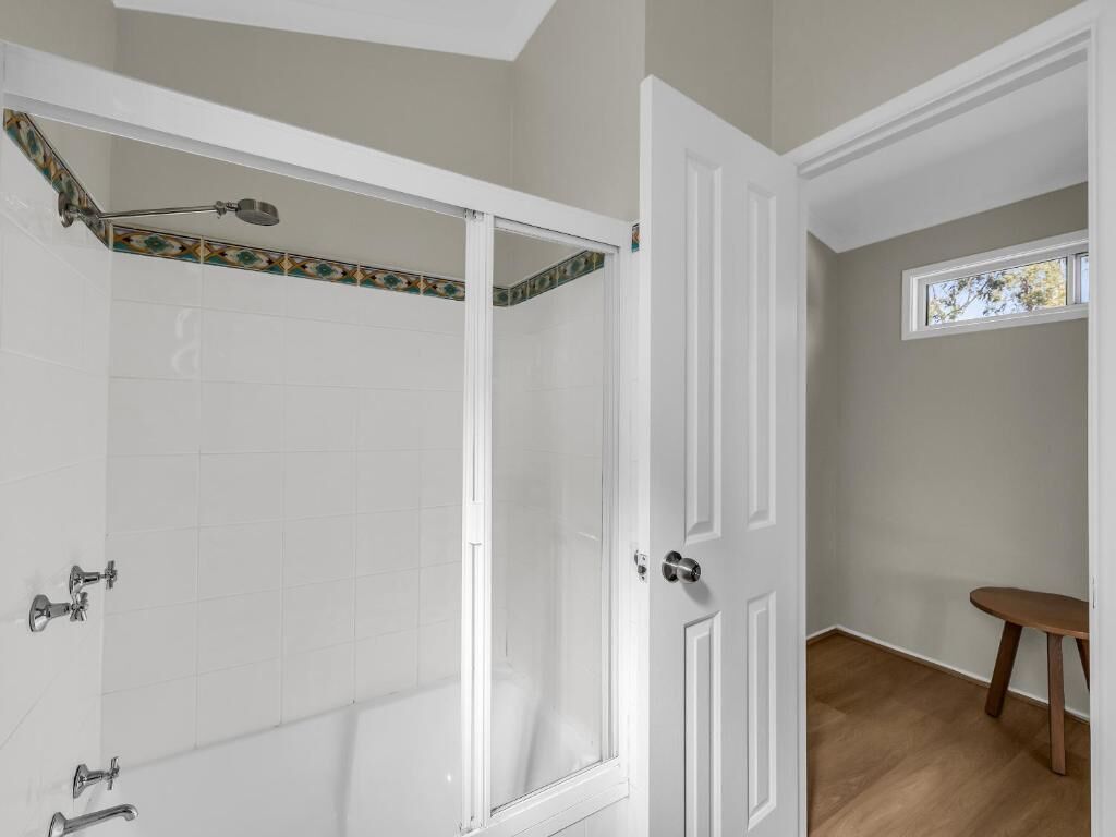 A bathroom with white tiled walls, a shower with a glass door, and a wooden floor.