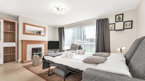 Un dormitorio moderno con cama, mesitas de noche, chimenea y un ventanal grande con cortinas.