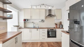 Una cocina moderna con armarios blancos, un refrigerador de acero inoxidable y una encimera de madera.