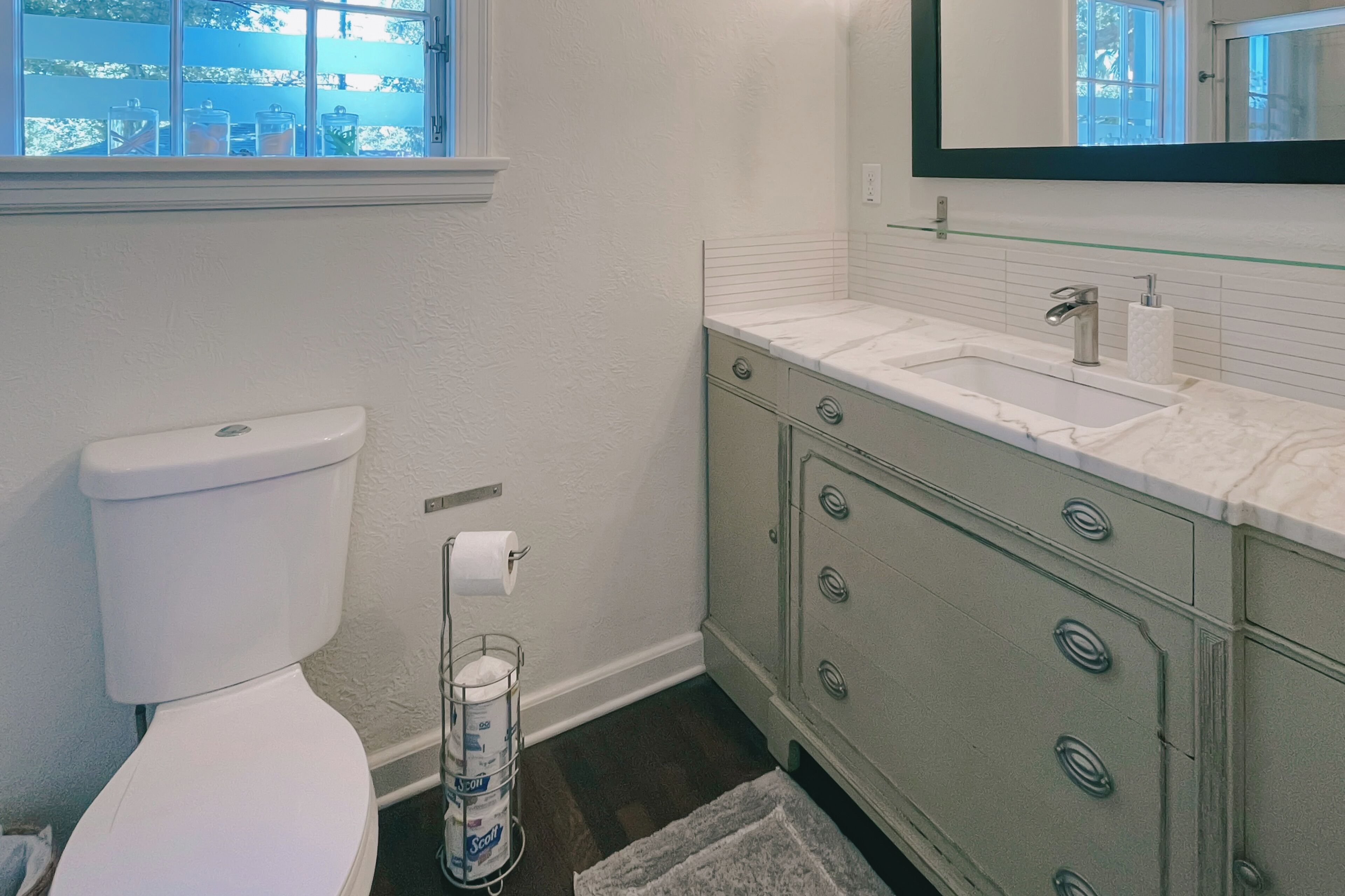 Un baño con inodoro blanco, cabina de ducha de vidrio y tocador con encimera de mármol.