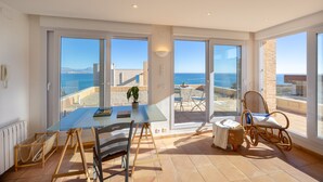 En rummelig balkon med krystalklart havudsigt, et glasbord med stole og en fletstol.