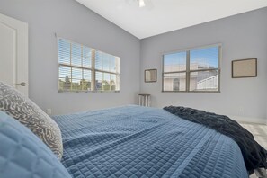 A bedroom with a bed, two windows with blinds, a door, and a small stool. - 6B Waterfront Game Room Pool Hot Tub Dock (Palm Harbor)