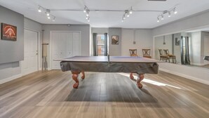 Een kamer met een pooltafel, houten vloeren, een deur en een spiegel aan de muur.