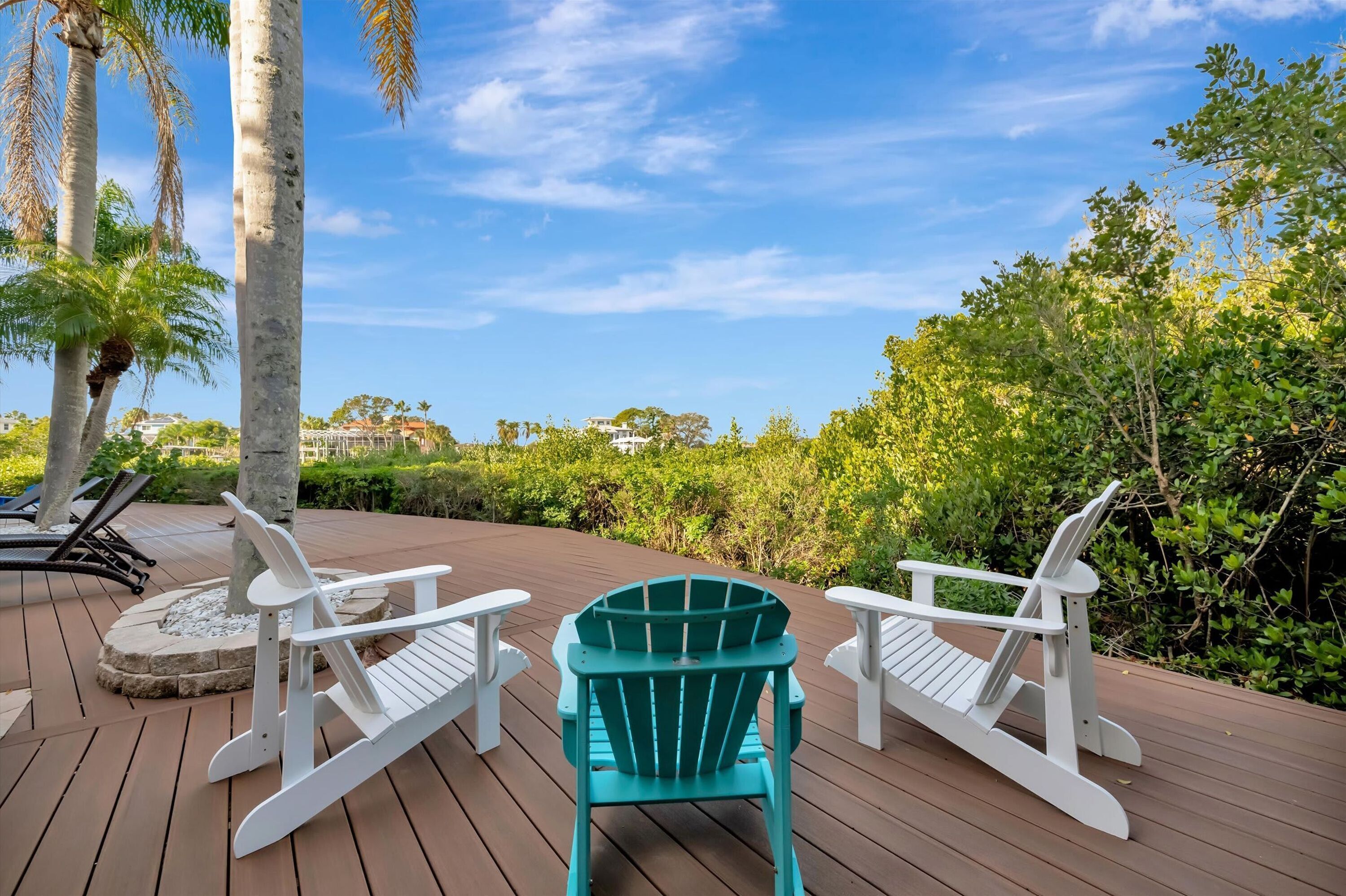 A wooden deck with two white Adirondack chairs and one teal Adirondack chair.