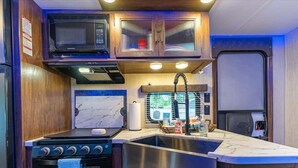 A compact kitchen with a microwave, stove, sink, and wooden cabinets. - RV in Tampa Great Location Cost pet Friendly (Tampa)