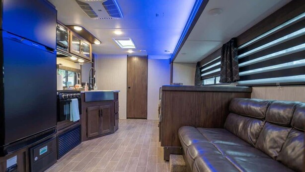 A compact RV interior with a kitchenette, a leather sofa, and a sliding door leading to a bathroom. - RV in Tampa Great Location Cost pet Friendly (Tampa)