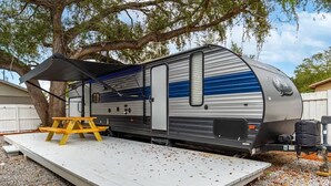 A recreational vehicle parked on a gravel surface with a picnic table and a canopy. - RV in Tampa Great Location Cost pet Friendly (Tampa)