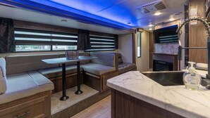 A compact RV interior with a kitchenette, seating area, and a window providing natural light. - RV in Tampa Great Location Cost pet Friendly (Tampa)