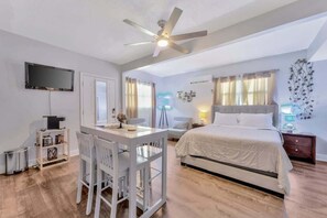 A bedroom with a bed, a desk, and a chair. There is a ceiling fan, a TV mounted on the wall, and a window with curtains. - Cozy Suite Full Amenitie s pet Friendly (Tampa)