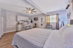 A bedroom with a large bed, a desk with chairs, a kitchenette, and a ceiling fan. - Cozy Suite Full Amenitie s pet Friendly (Tampa)