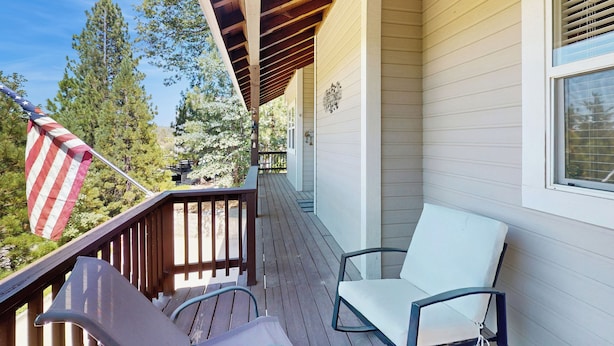 A wooden deck with a white chair and a metal chair, an American flag, and a window with blinds. - Walk to Lake Arrowhead! Family Home w/ Games (Lake Arrowhead)