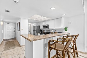 A modern kitchen with white cabinets, a granite countertop, and a central island with bar stools. - 2BR w/ Gulf-View Balcony: Suntide III - Unit 404 (South Padre Island)