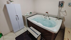 Un baño con bañera, inodoro, armario, una planta pequeña y un calentador de pared.