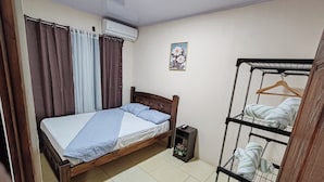 Un dormitorio con cama, armario, aire acondicionado y una pequeña estantería con toallas.