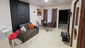 Una sala de estar con un sofá, una mesa de comedor con sillas, una mesita con una planta y una pared negra con textura.