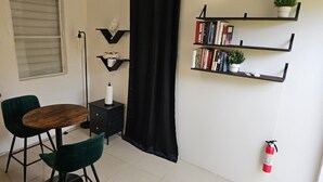 A small, modern room with a dining table, two chairs, a black curtain, a bookshelf, and a fire extinguisher. - Ponce Pueblo Central Apt (Ponce)