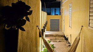 A narrow alleyway with a hammock, potted plants, and a building with a shuttered door. - Ponce Pueblo Central Apt (Ponce)