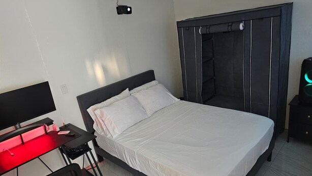 A bedroom with a bed, a desk with a computer, and a wardrobe. - Ponce Pueblo Central Apt (Ponce)