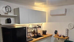 A compact kitchen with a black refrigerator, wooden countertop, and two green chairs around a small wooden table. - Ponce Pueblo Central Apt (Ponce)