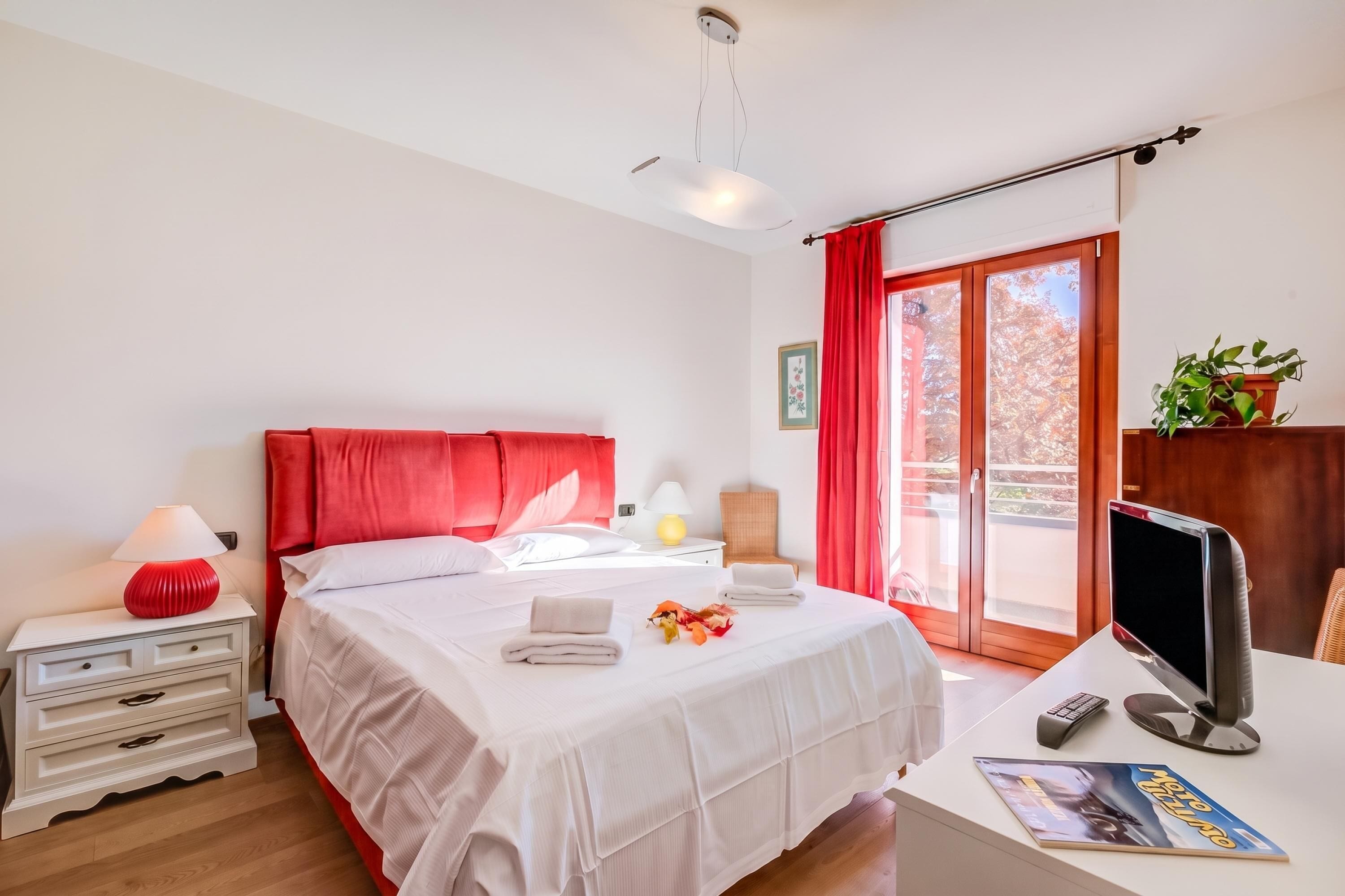 Una camera d'albergo con un letto, un comodino, una lampada e una scrivania con un computer.