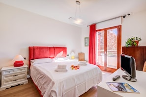 Quarto de hotel com cama, mesa de cabeceira, abajur e escrivaninha com computador.