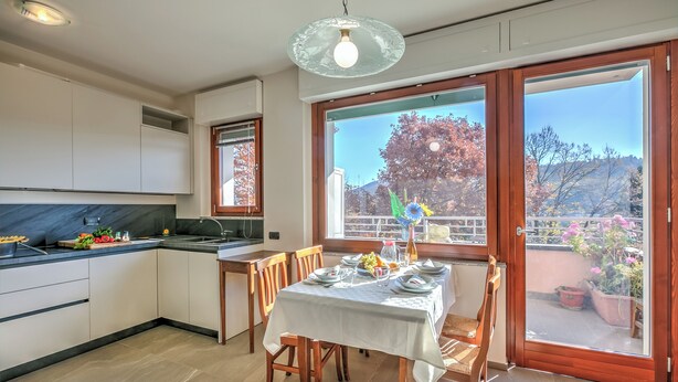 A modern kitchen with a dining area, large windows, and a view of the outdoors. - Appartamento Residenza Chiara: Sunny Balcony and Mountain View (Laveno Mombello)