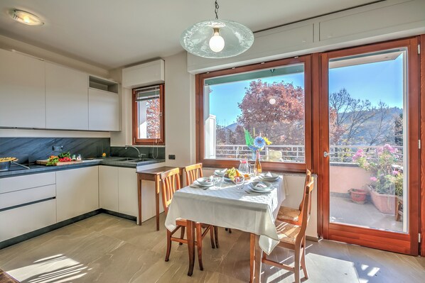 A modern kitchen with a dining area, large windows, and a view of the outdoors. - Appartamento Residenza Chiara: Sunny Balcony and Mountain View (Laveno Mombello)