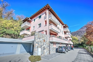 Un hotel de varios pisos con balcones, fachada de piedra y zona de estacionamiento.