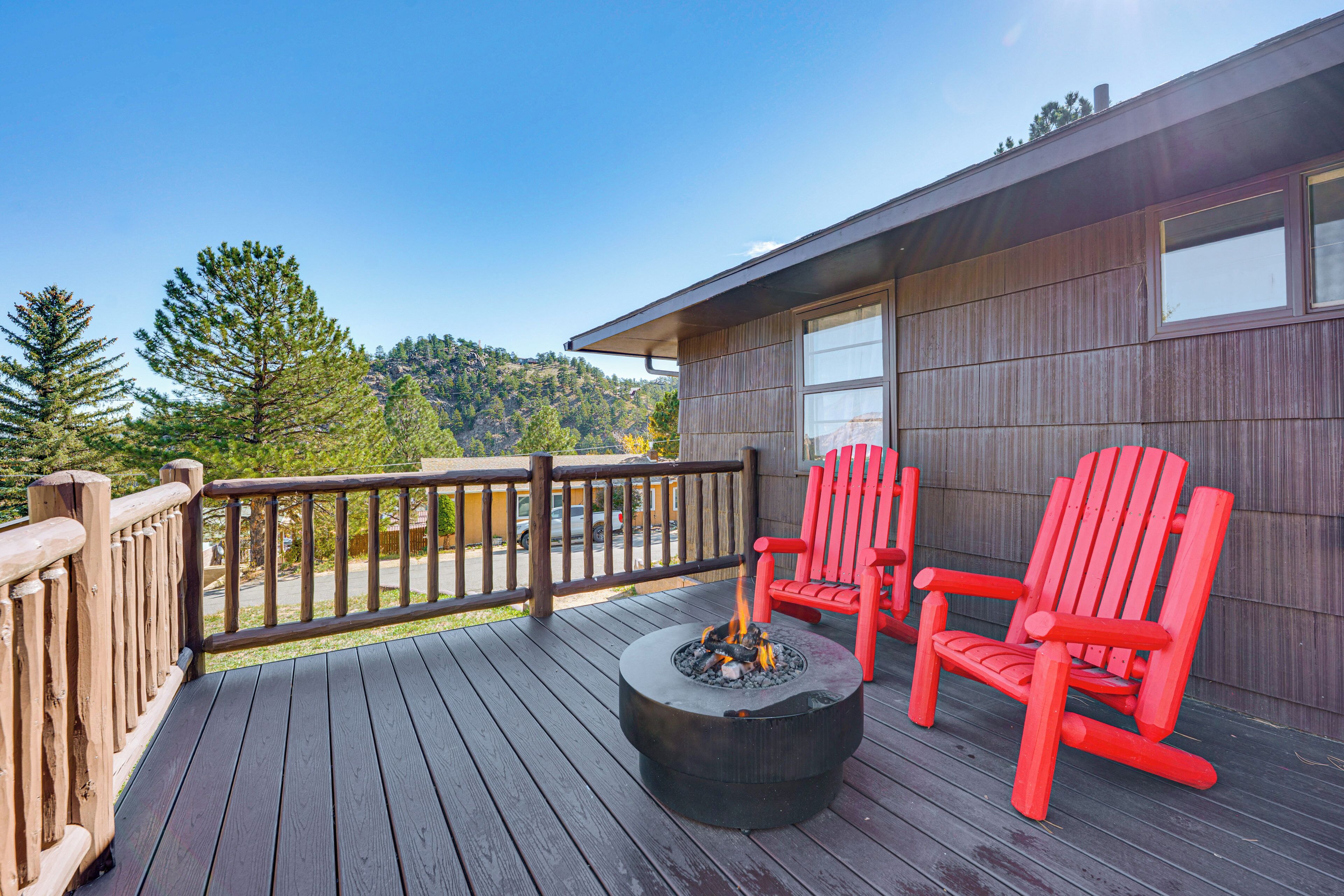 A deck with a fire pit, two red Adirondack chairs, and a view of a forested hillside.