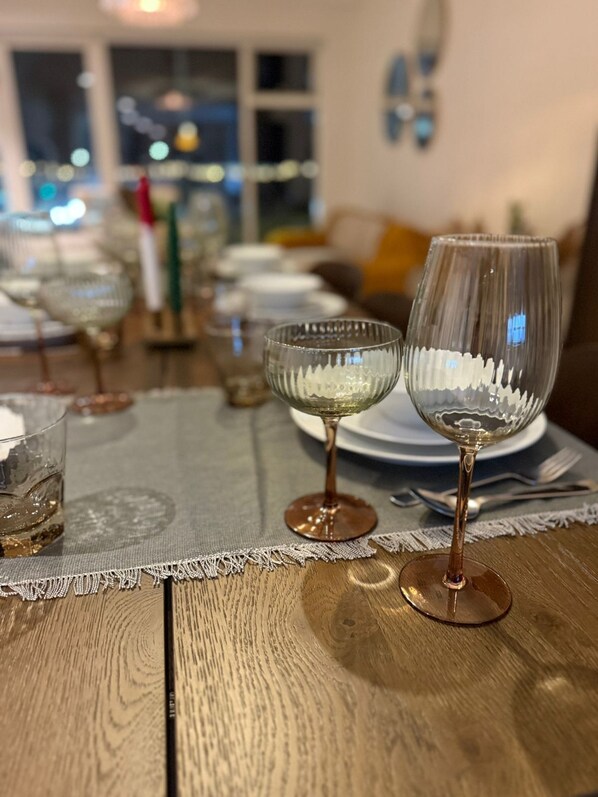 Une table à manger, ornée de verres à vin et d’assiettes, est placée sur une table en bois recouverte d’un chemin de table en dentelle.