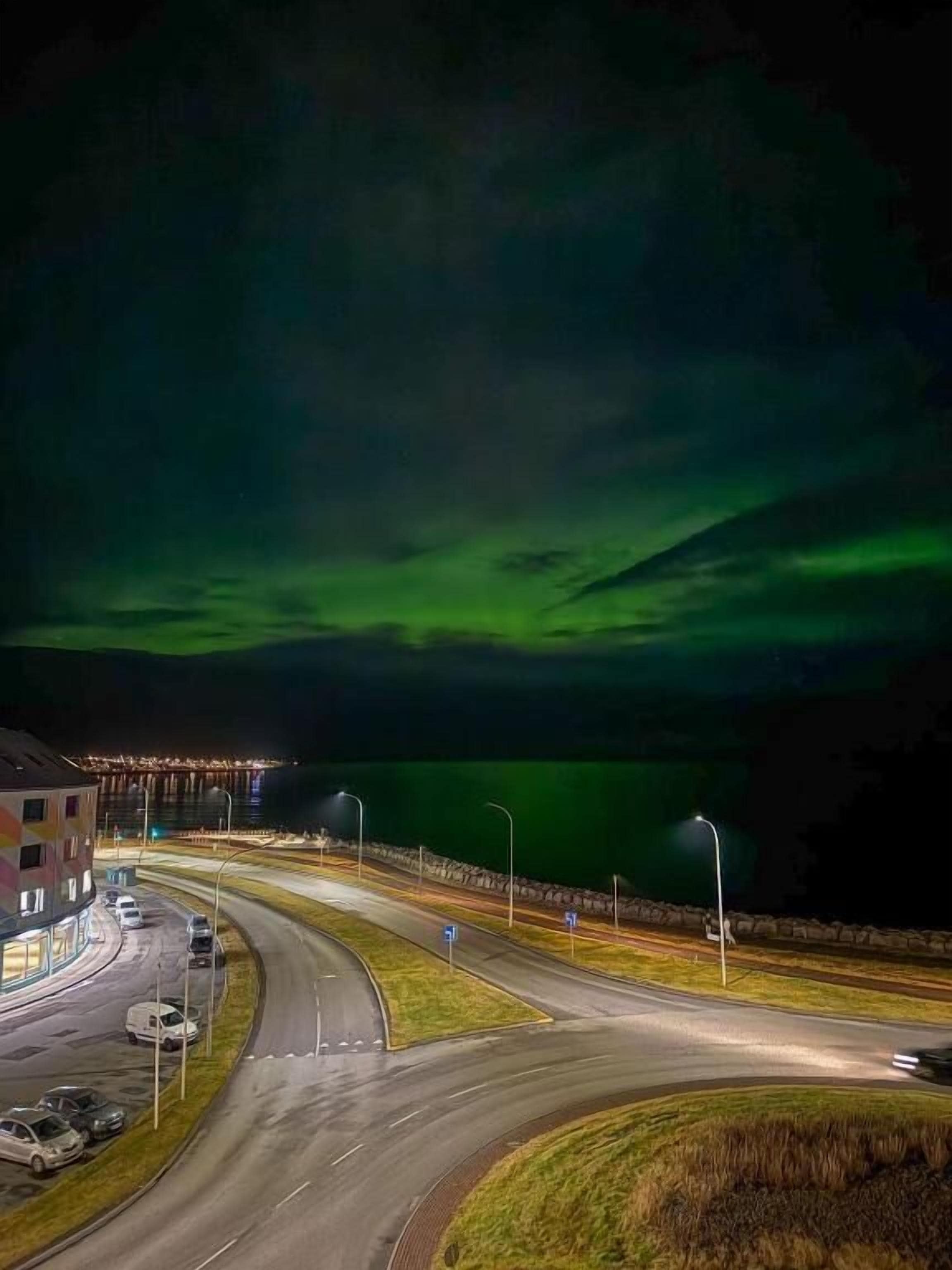 A nighttime view of a road with a green aurora display in the sky.