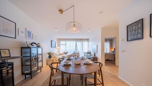 A modern dining area with a round table set for four, surrounded by chairs. A chandelier hangs from the ceiling, and the room has a clean, minimalist design with white walls and wooden flooring. - Ice Apartments (Reykjavík)