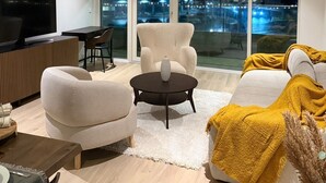 A modern living room with a large TV, comfortable seating, a dining area, and a view of a cityscape at night. - Ice Apartments (Reykjavík)