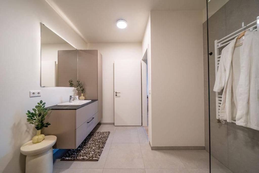 A modern bathroom with a toilet, sink, mirror, and shower area.