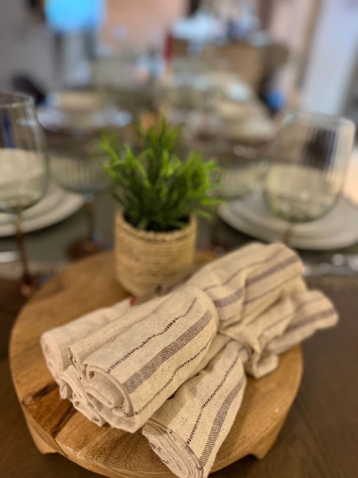 Una mesa de madera con una cesta tejida que contiene una planta verde, un paño doblado y un vaso.
