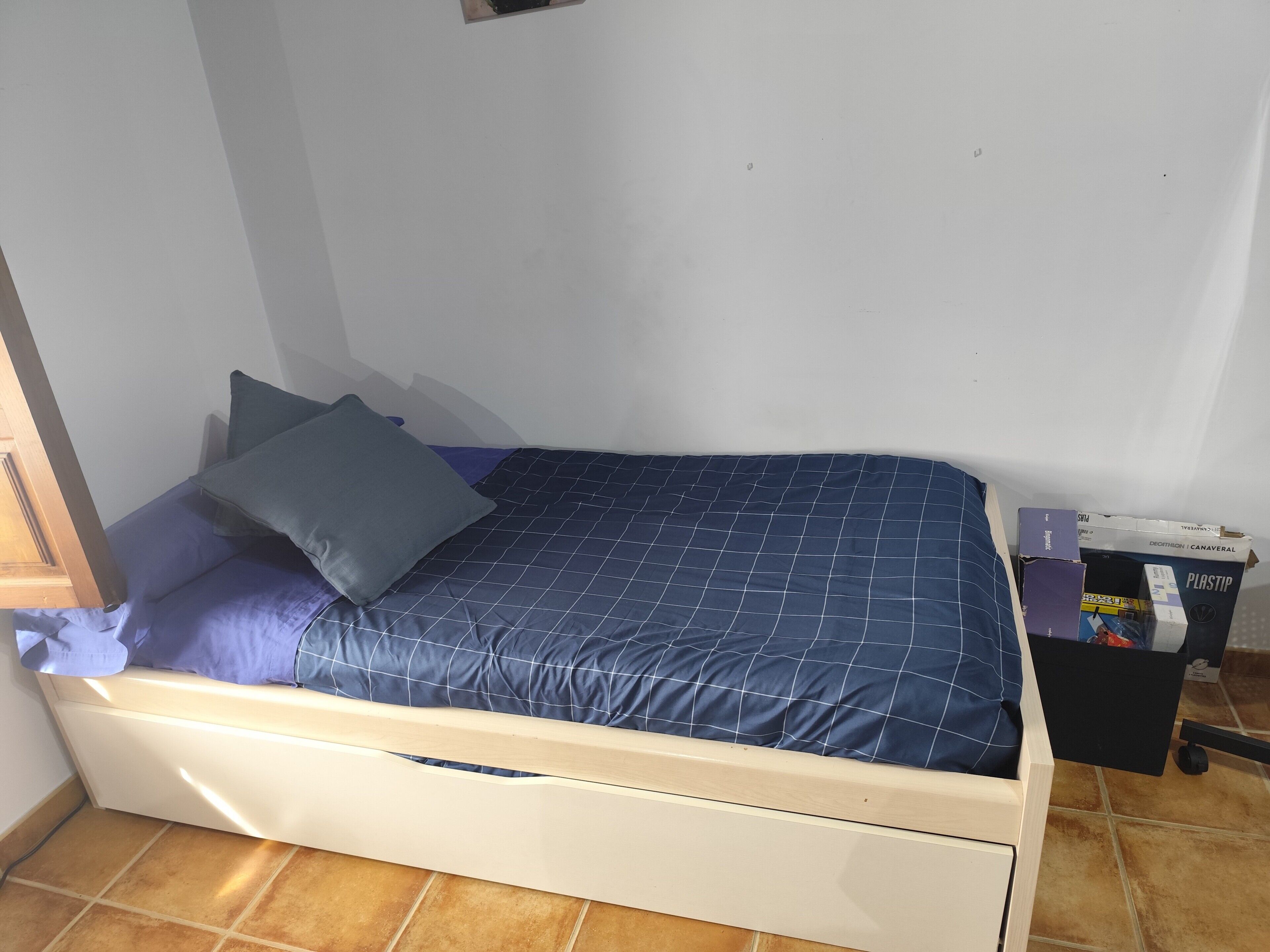 Una cama individual con cabecera, una mesita de noche de madera y un pequeño cofre.