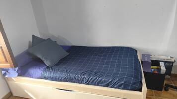 Una cama individual con cabecera, una mesita de noche de madera y un pequeño cofre.