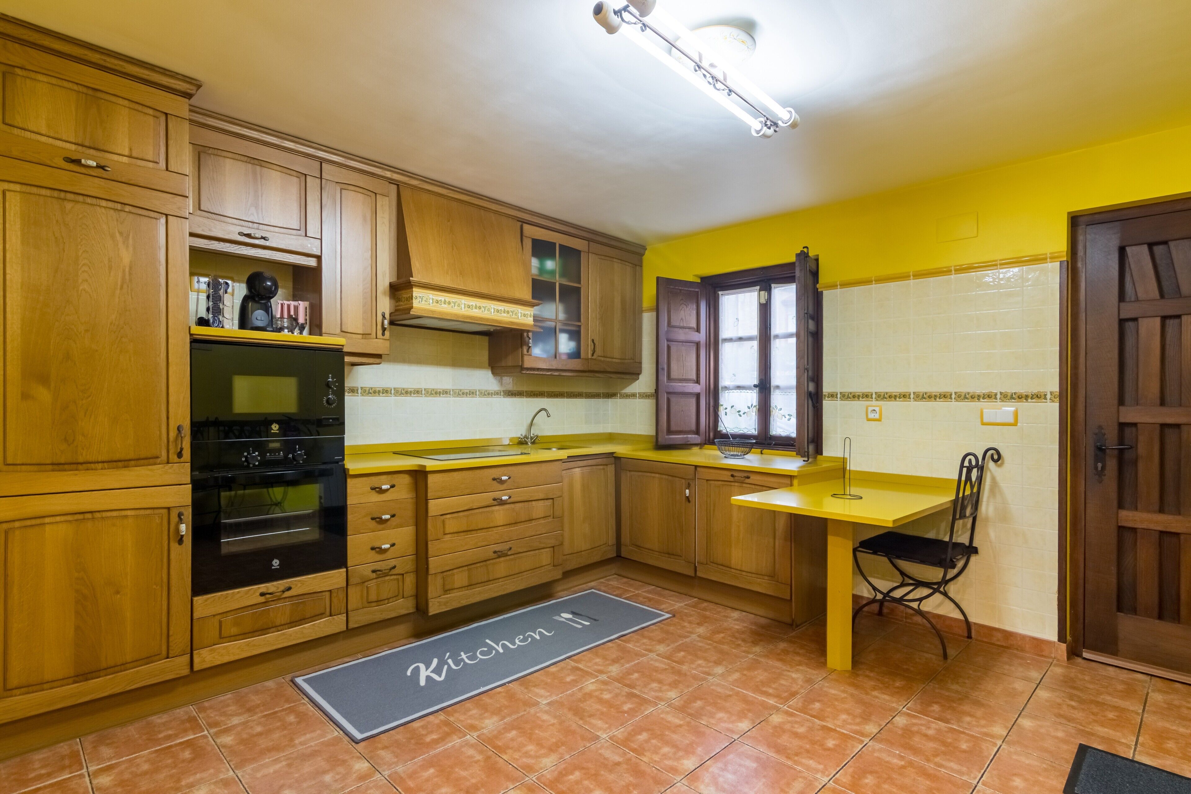 Una cocina con armarios de madera, horno negro, encimera amarilla y ventana con vistas.