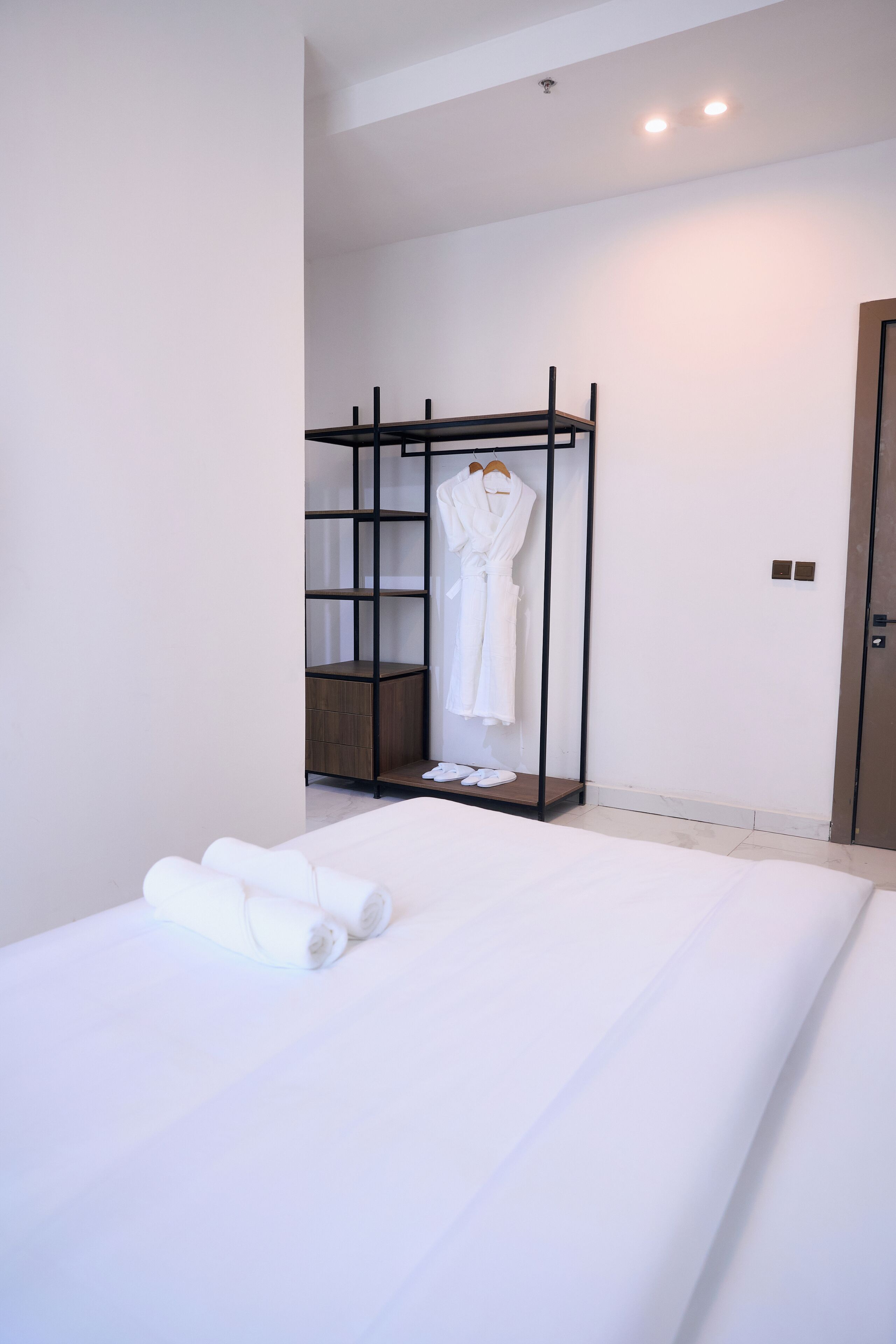 A hotel room with a large bed, a wooden wardrobe, and a robe hanging on the wardrobe.