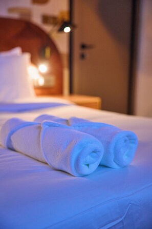 A neatly made bed with rolled white towels and a visible wooden headboard. - Azusa Hotels and Apartment  (Abuja)