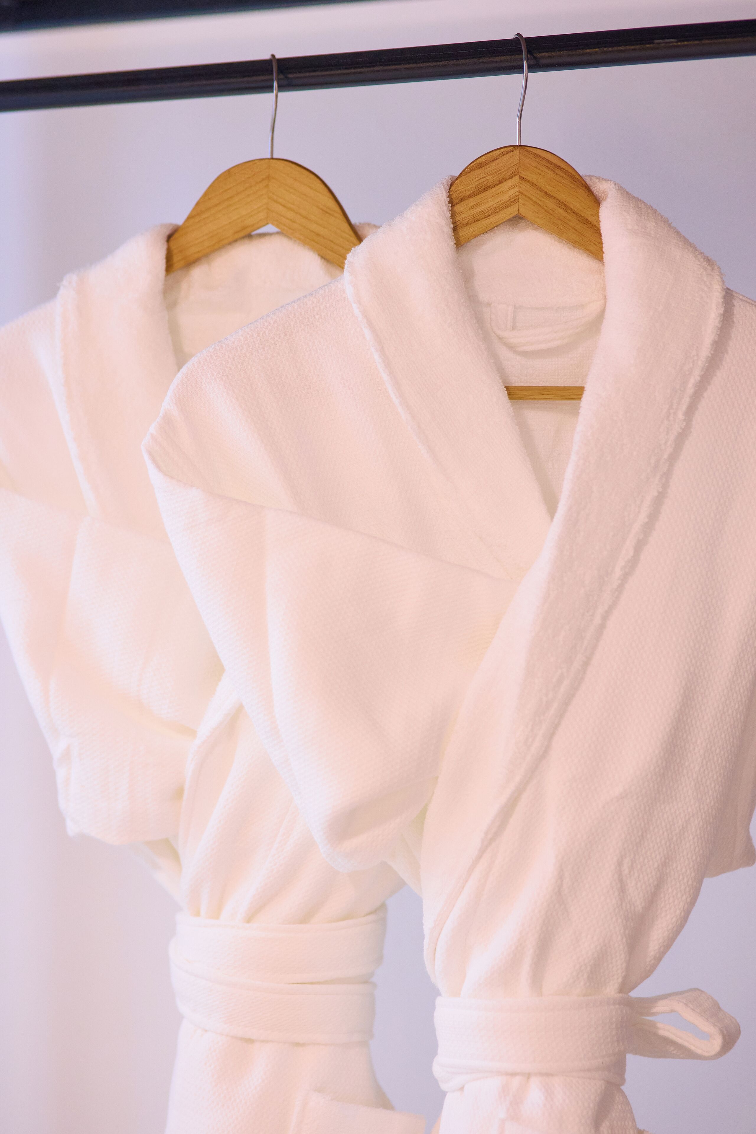 Two white bathrobes hanging on a wooden hanger.