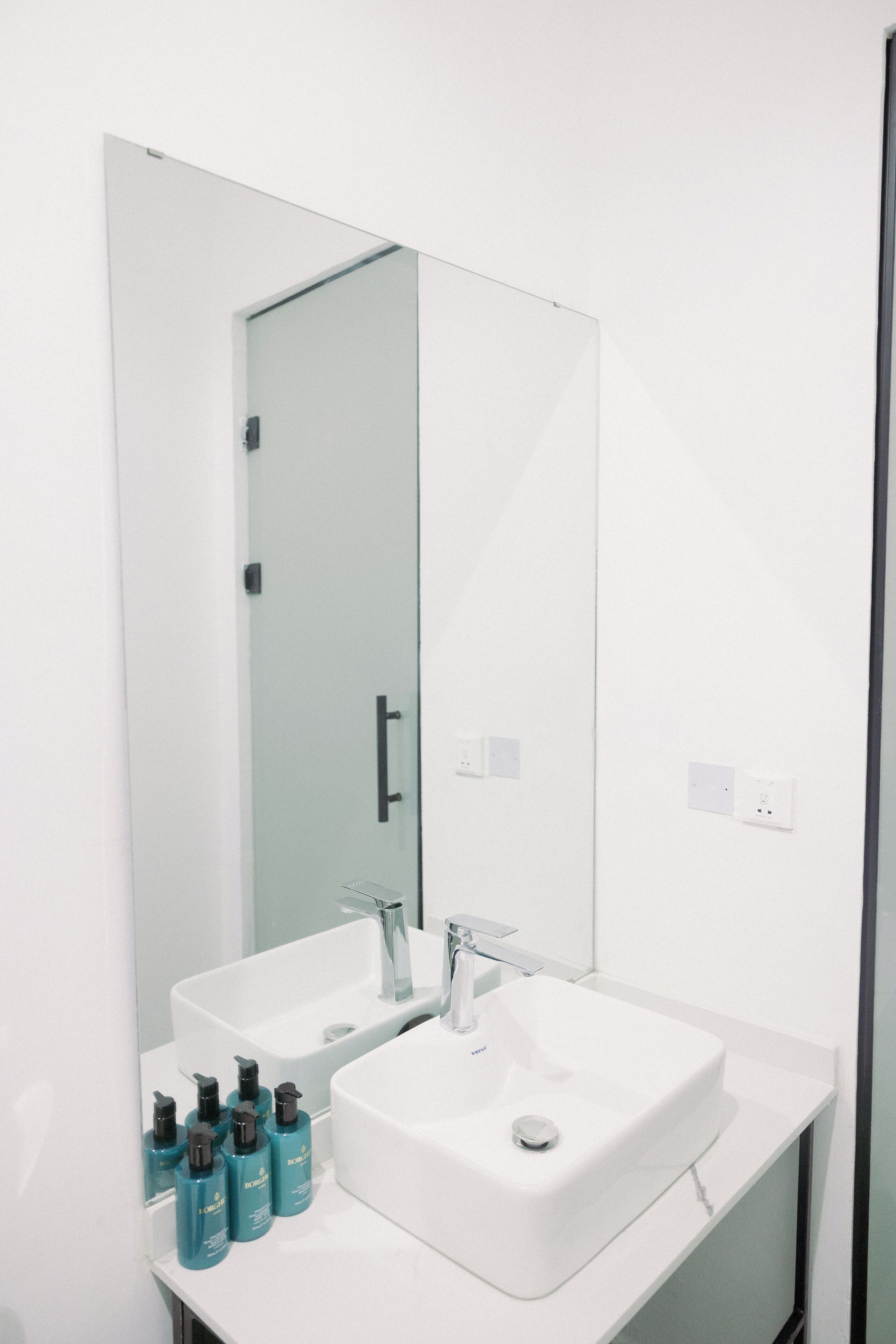 A modern bathroom with a white sink, a large mirror, and a glass shower door.