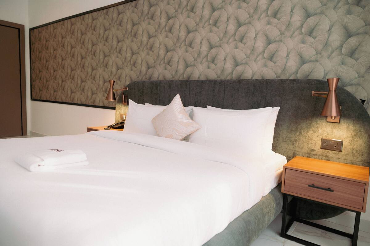 A neatly made bed with white linens, a grey headboard, and two bedside lamps.