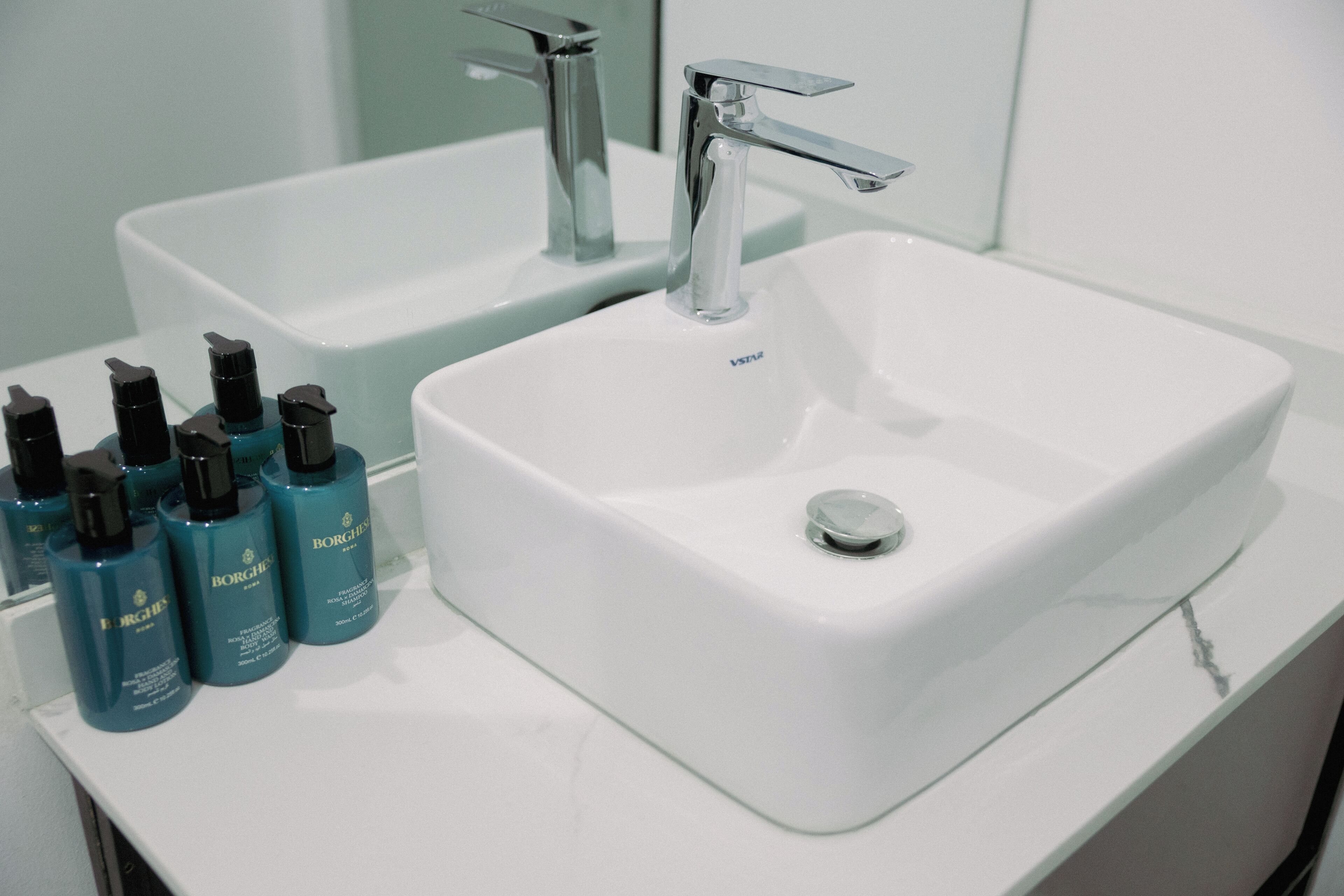 A bathroom with a white sink, two faucets, and several Borghese branded bottles on the counter.