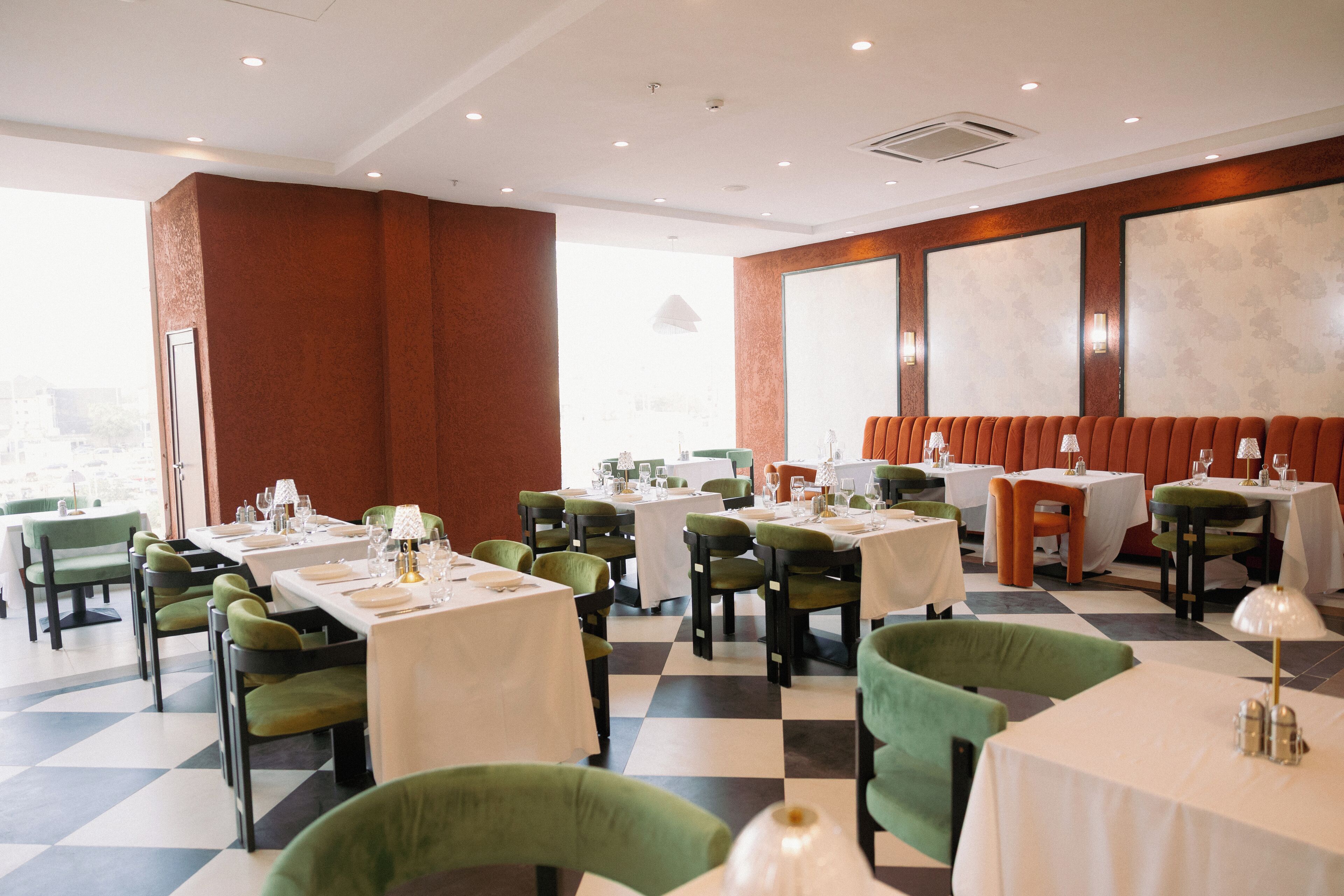 A restaurant with checkered flooring, green upholstered chairs, and white tablecloths.