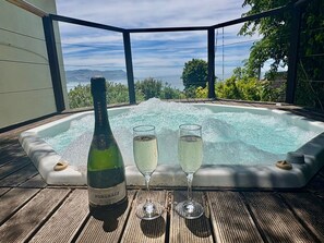 Een hottub met een fles Pongeracz Brut champagne en twee glazen op een houten terras, met uitzicht op bergen.