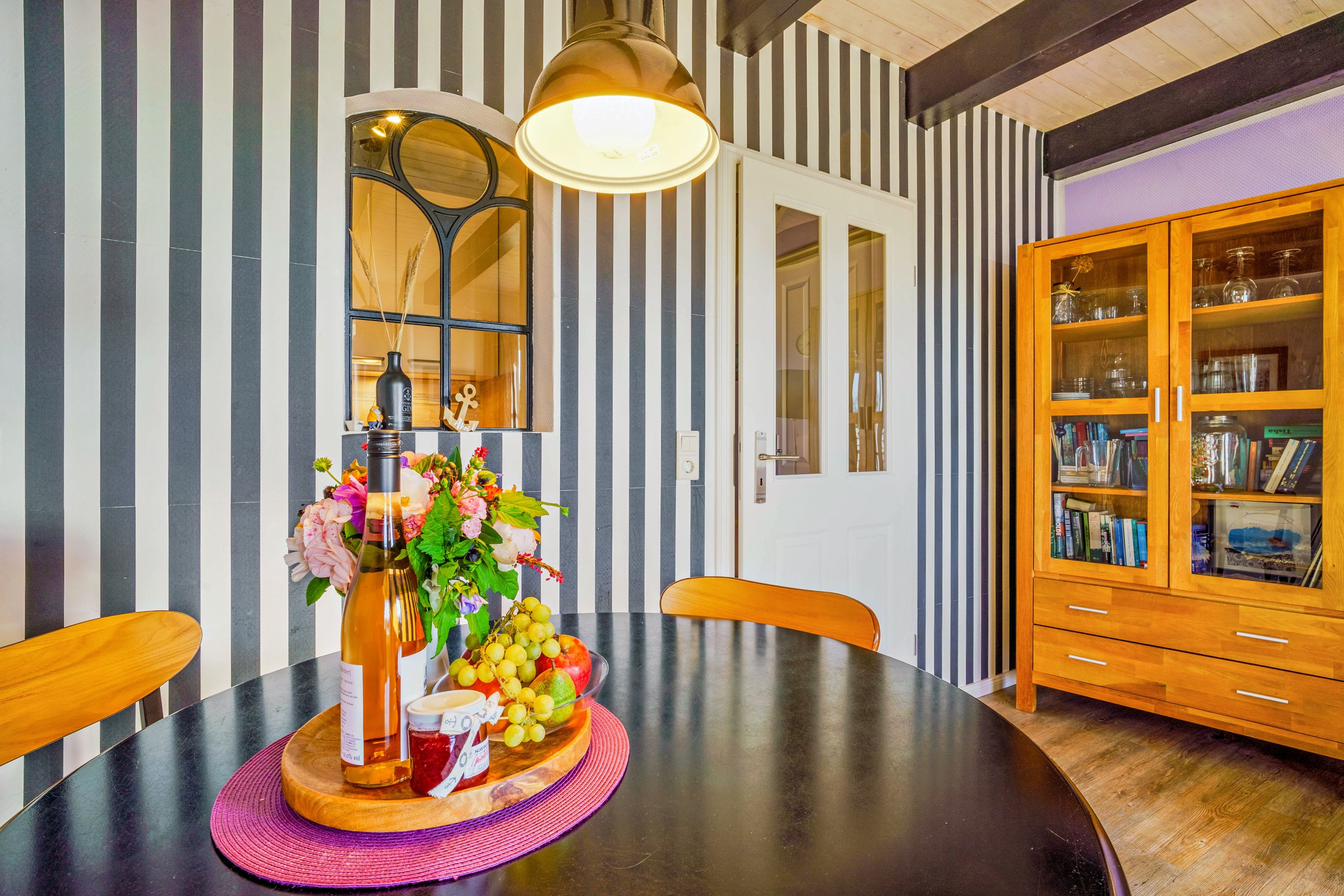 Ein Essbereich mit einem runden Tisch, Stühlen, einer Blumenvase und einer Holzkommode mit Glastüren.