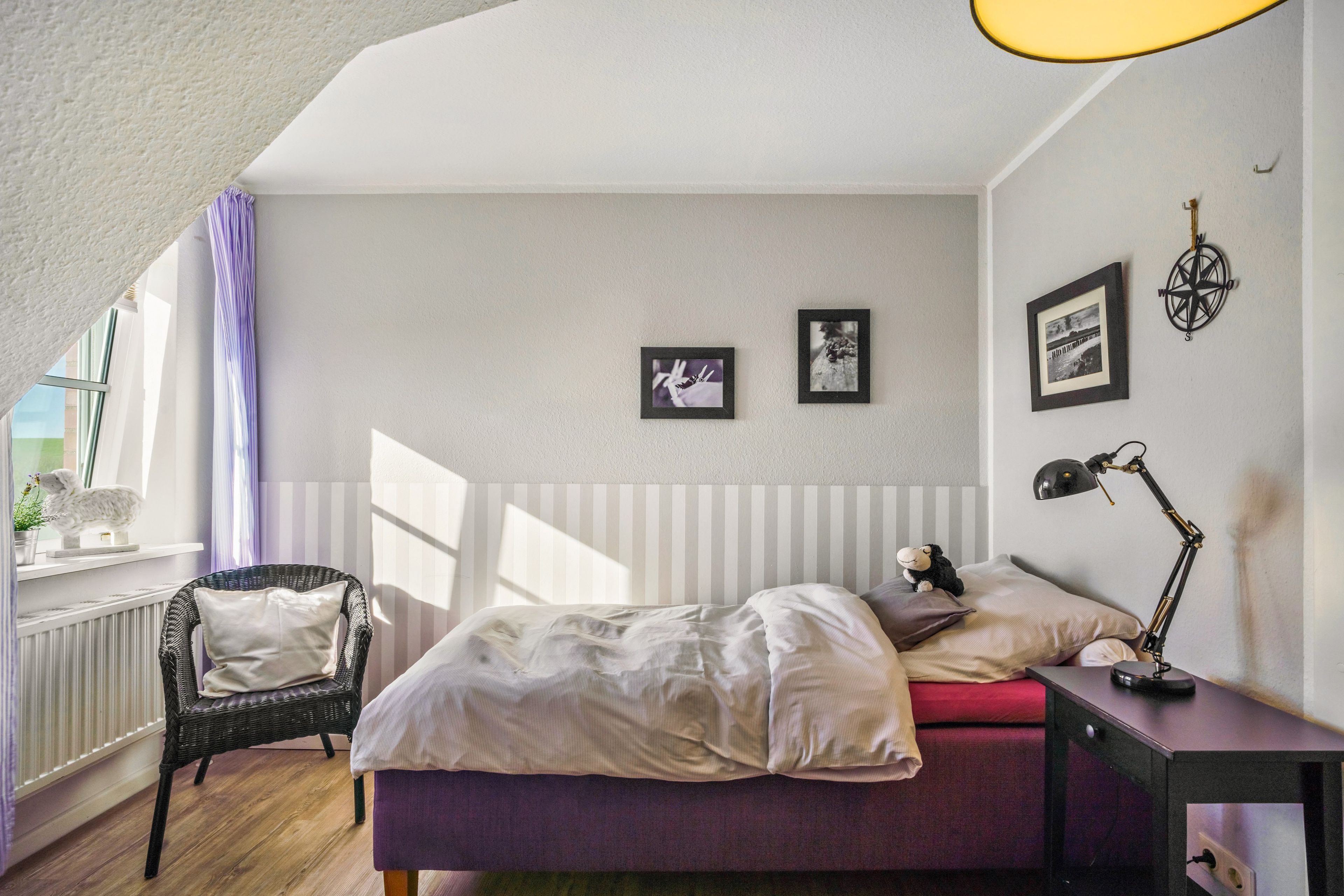 A bedroom with a bed, a chair, a desk with a lamp, and a window with curtains.
